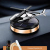 Parfum auto solaire doré rotatif avec boîtier noir et applicateur en bois sur une surface sombre.