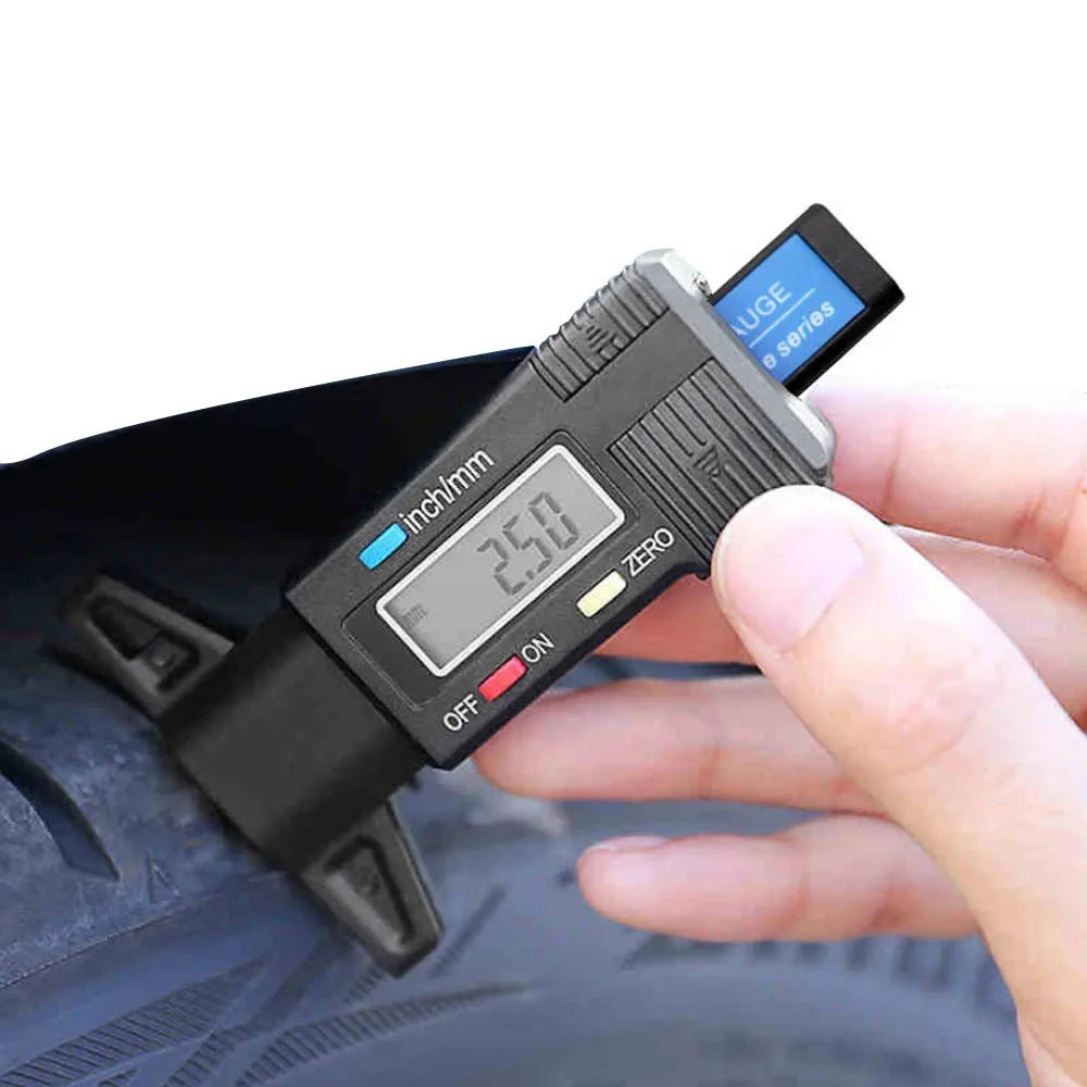 A hand holds a digital tyre depth gauge measuring 2.50 inches on a dark tire.
