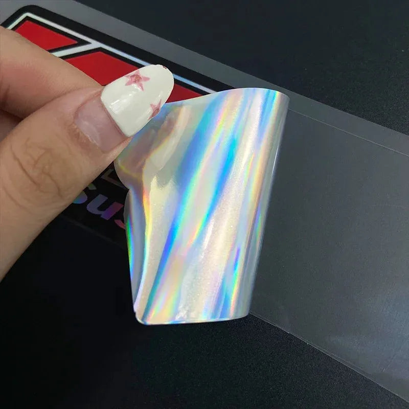 A close-up of a clear, iridescent racing suspension decal for motorcycles being held by a finger.