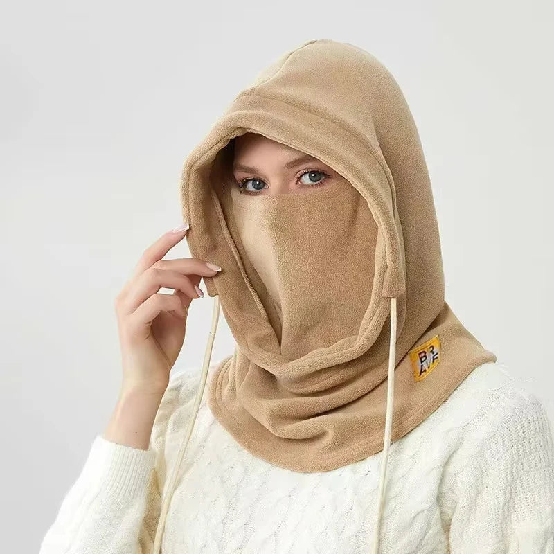 Una mujer vistiendo una balaclava y bufanda cortavientos beige sobre un suéter blanco.