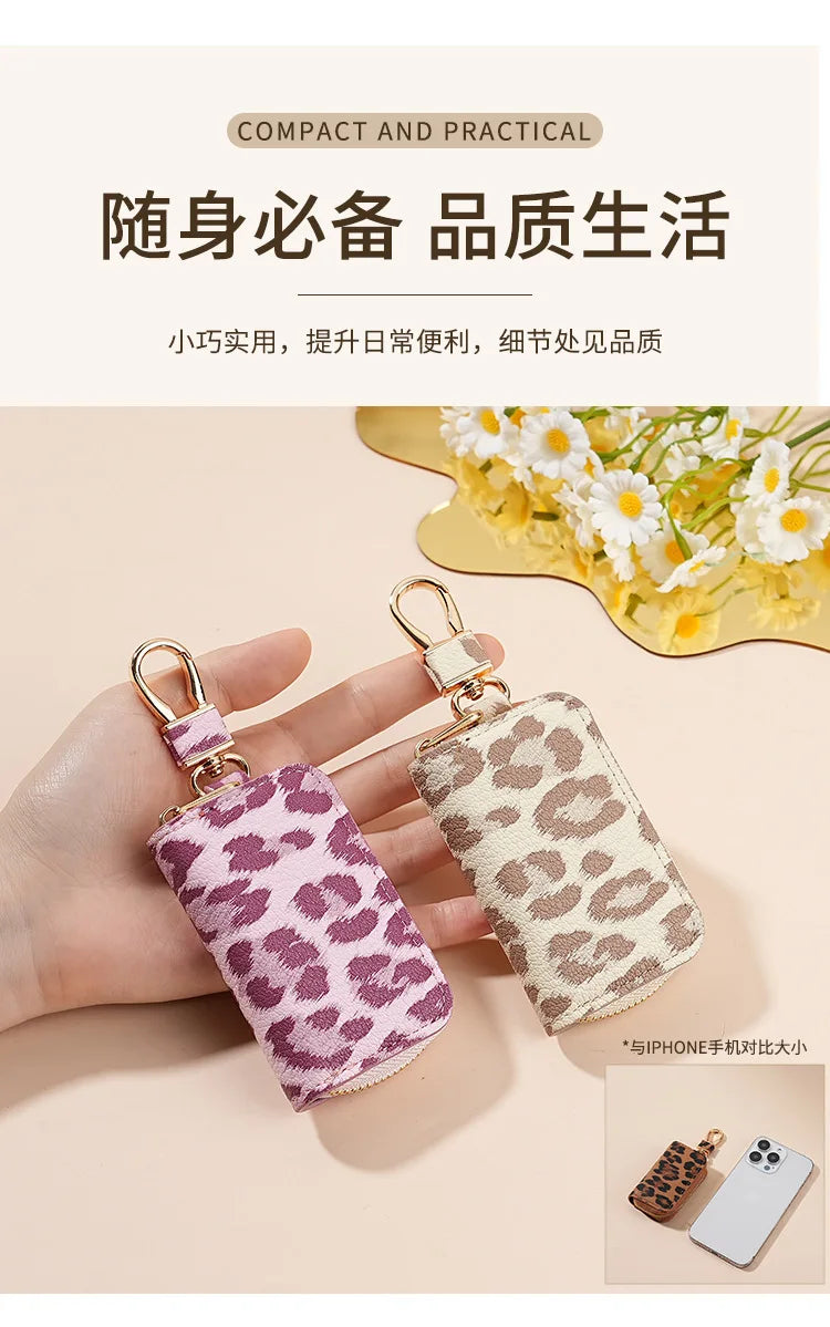 A pair of small, pink and beige leopard print car key holders are shown being held by a hand.