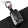 A black carbon fiber button cover for a car key, featuring a silver clasp and a red and blue accent.