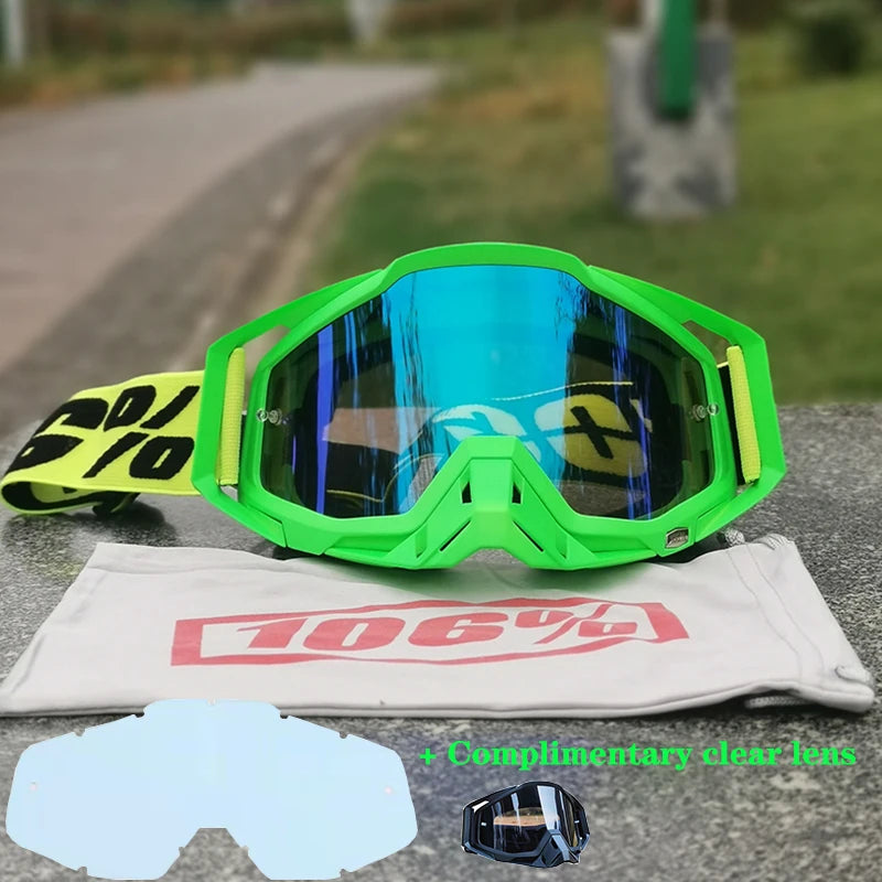 A pair of bright green motocross goggles resting on a gray surface, with an additional clear lens included.