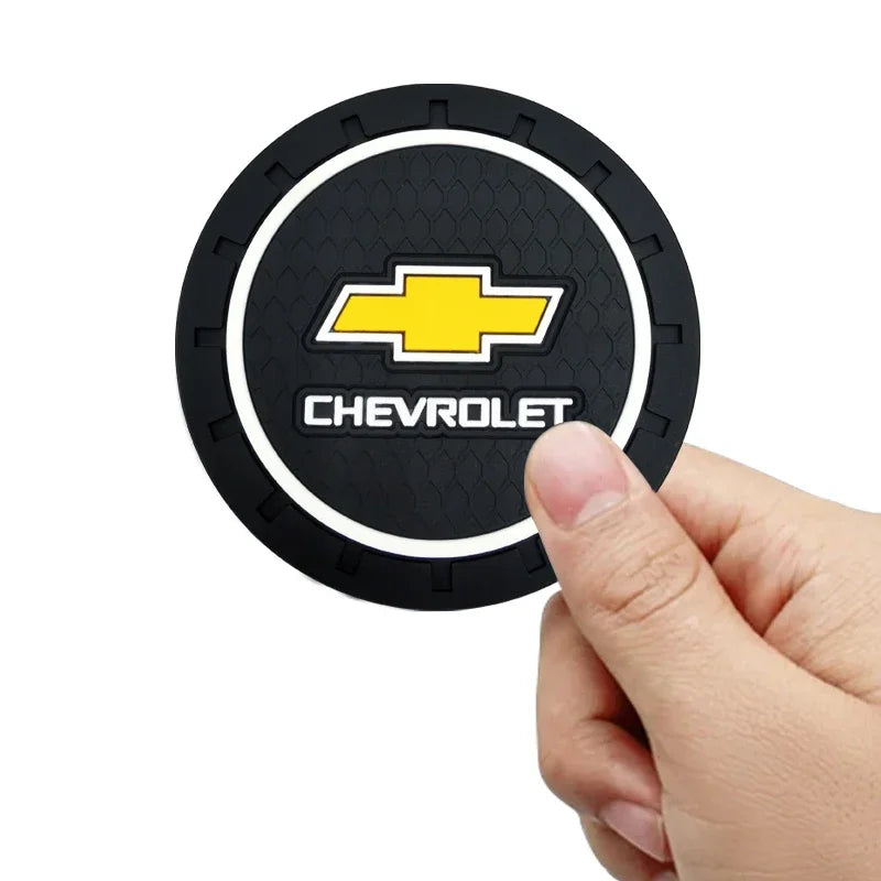 A hand holds a black car anti-slip coaster with a yellow Chevrolet emblem and text.