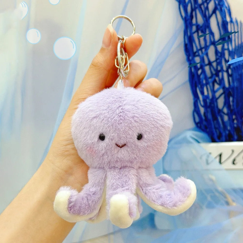 A soft purple plush bunny keychain with white accents and a gold ring is being held by a hand.