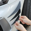 A hand is adjusting black universal car spoiler fins on a white vehicle's front bumper.