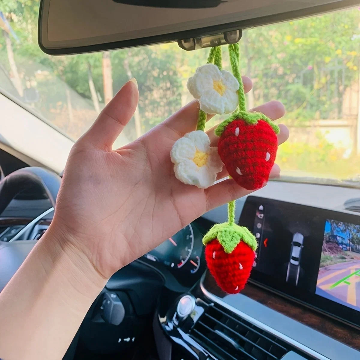 Une main tient un pendentif de clé en crochet de fraise fait main avec des fleurs blanches, accroché dans l'intérieur d'une v