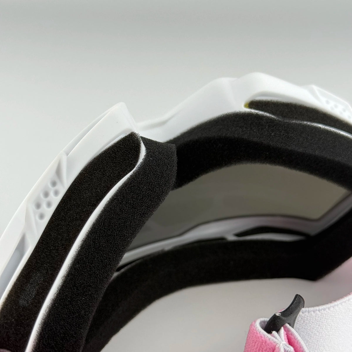Close-up view of white and black off-road motorcycle goggles with pink accents