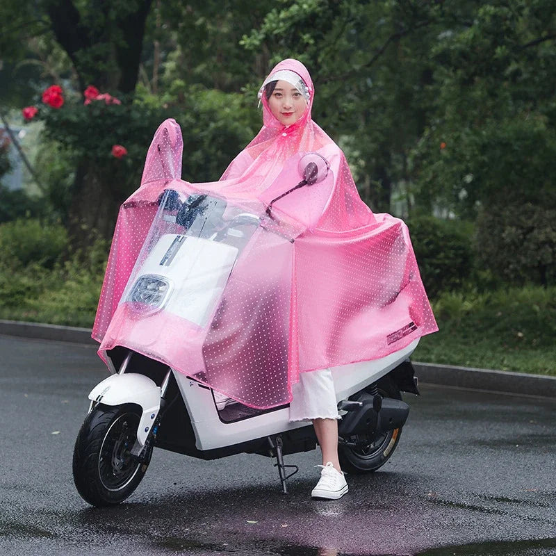 A woman wearing a pink transparent windproof motorcycle rain poncho is riding a white scooter on a wet road.