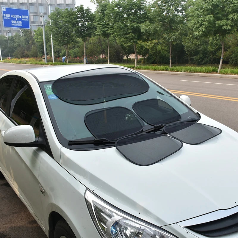 A white car with tinted side windows and a black sun shade mesh installed on the windshield.
