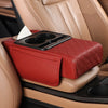 A red quilted car armrest cushion with a tissue holder is placed on a tan leather car seat.