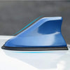 Blue shark fin universal car antenna amplifier mounted on a white surface.