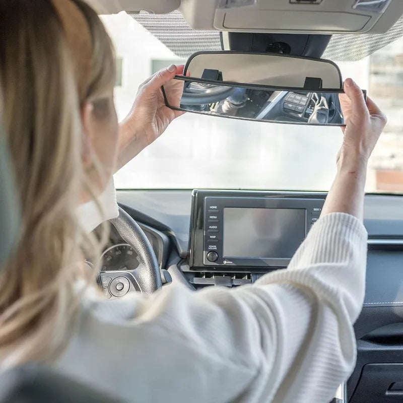 A person is adjusting a clip-on wide-angle rear view mirror on a vehicle's interior.