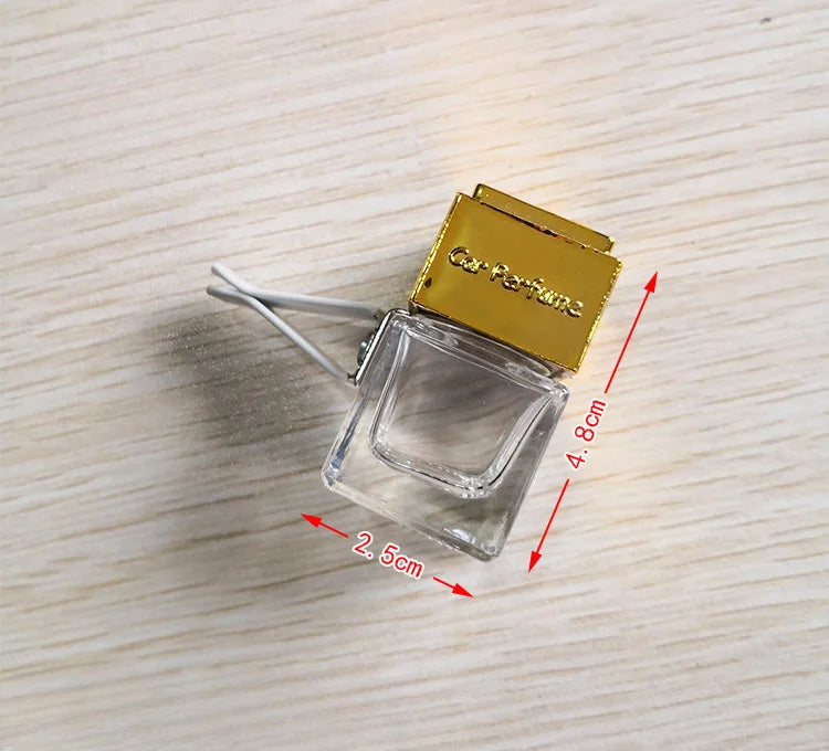 A clear glass bottle of car air freshener with a gold-colored cap resting on a wooden surface.