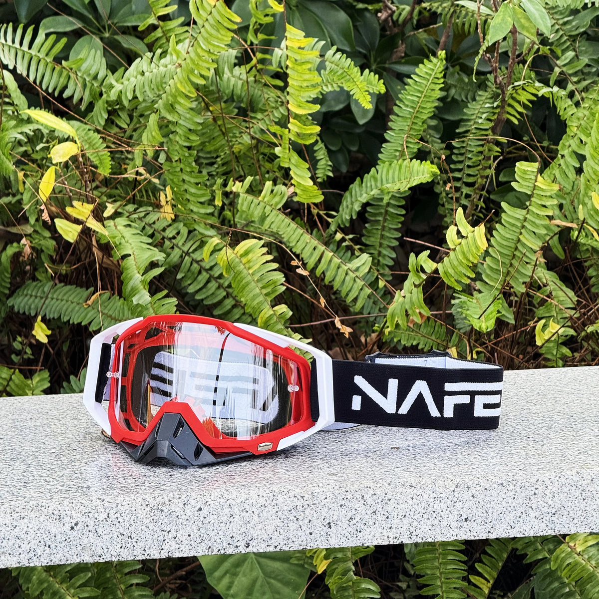 Ein Paar rot-schwarzer Motocross-Goggles auf einer hellgrauen Oberfläche.