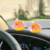 A decorative car rubber duck in yellow and pink with accessories resting on a car dashboard.
