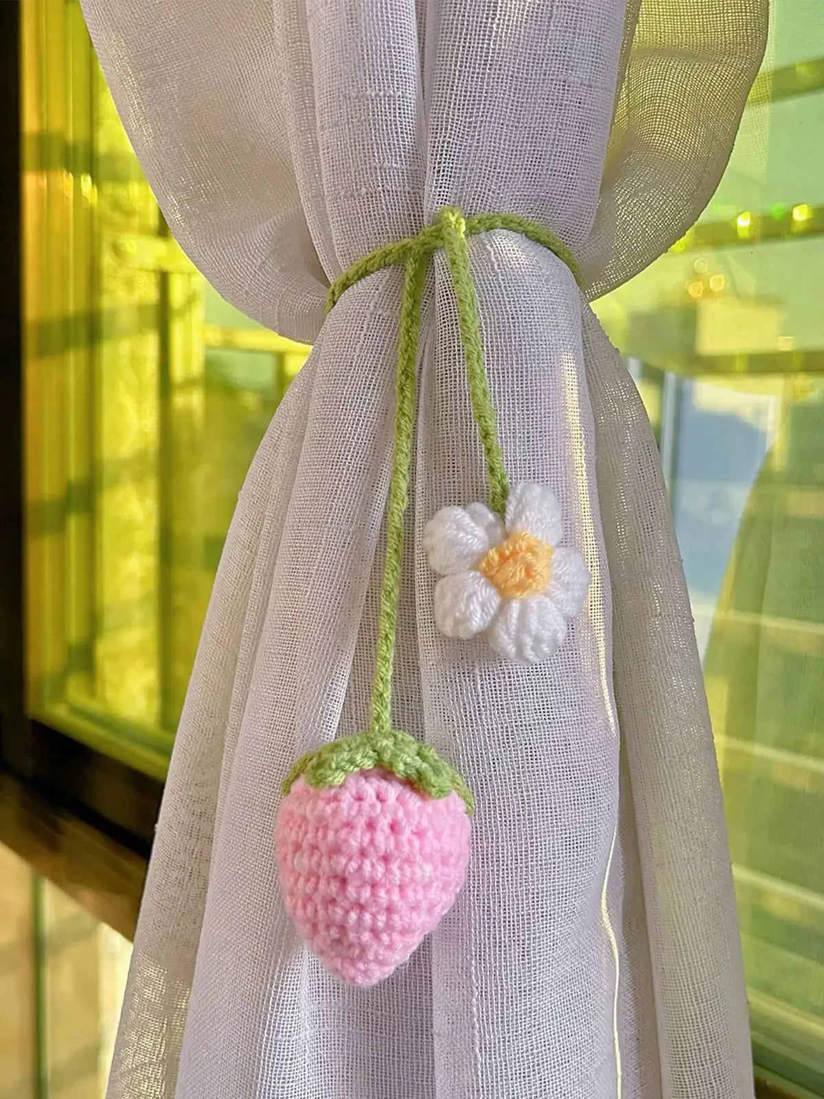 Charm de fraise crochet fait main, suspendu à un ruban de tissu blanc transparent.