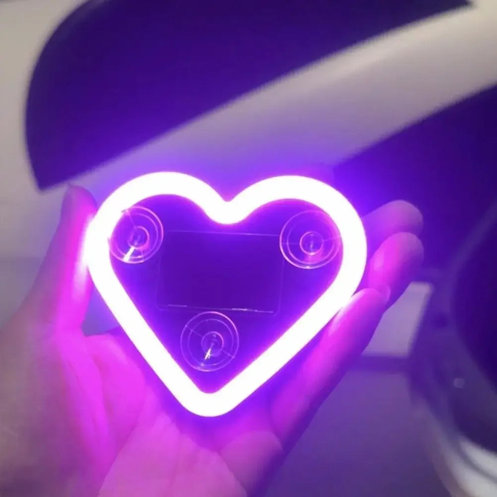 A hand holds a neon heart shaped light illuminating a dark window area.