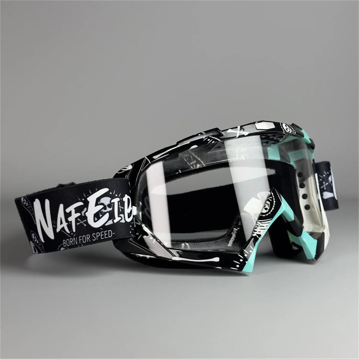A pair of black motorcycle off-road goggles with a clear lens and black strap are displayed against a gray background.
