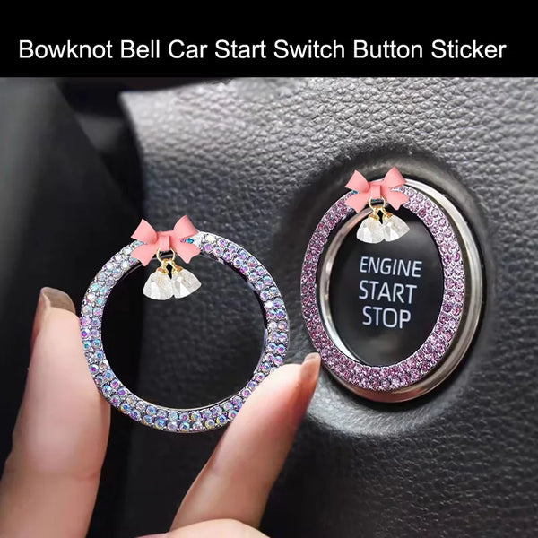 A hand holds a decorative rhinestone bow bell car start switch button sticker placed on a vehicle's ignition panel.