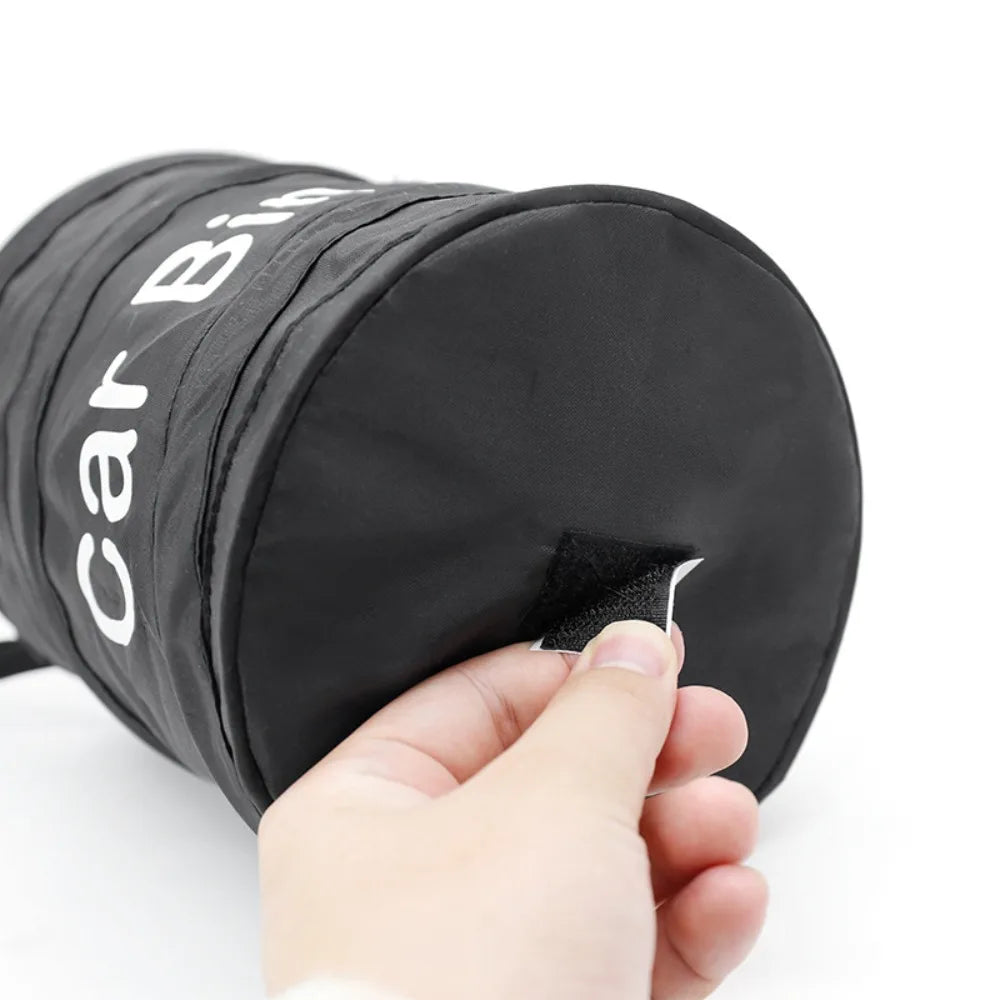 A hand is holding a black waterproof collapsible car trash can bag with white lettering on it.