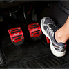 A foot wearing a black and gray athletic shoe rests on a car floor with red aluminum pedal covers visible.