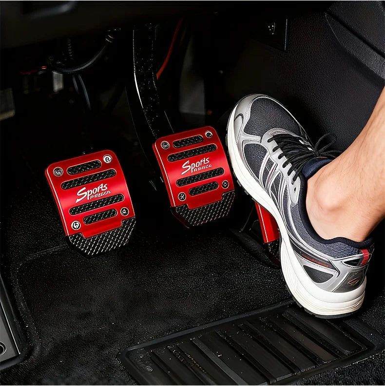 A foot wearing a black and gray athletic shoe rests on a car floor with red aluminum pedal covers visible.