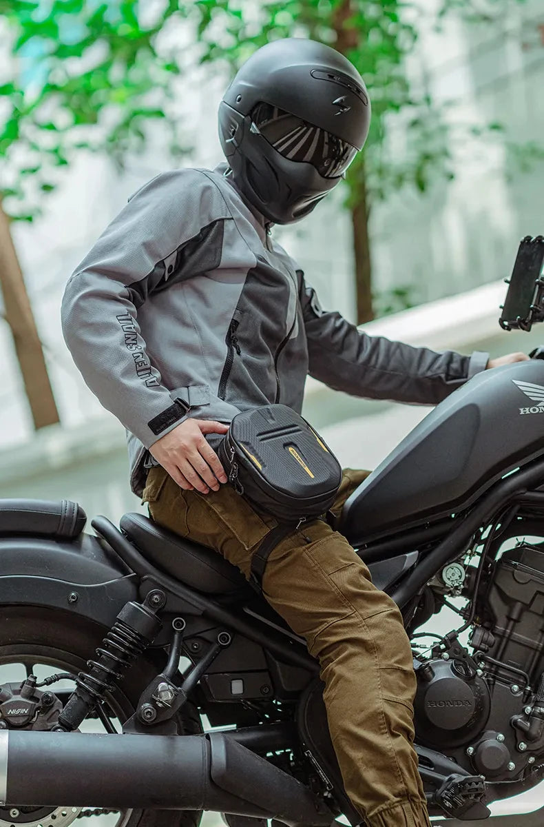 A person wearing a black helmet and gray jacket sits on a motorcycle with a brown fanny pack.