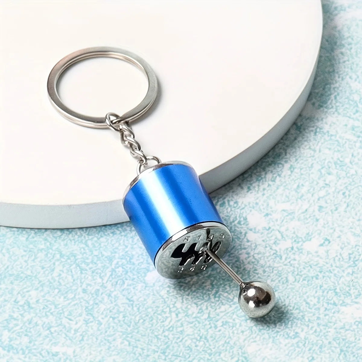 A blue cylindrical keychain with a silver ball attached, featuring a metal ring for modification or desk stress relief.