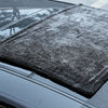 A dark gray microfiber cleaning cloth is placed on the hood of a car.