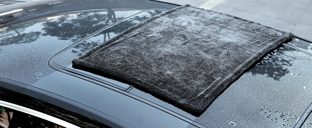 A dark gray microfiber cleaning cloth is placed on the hood of a car.