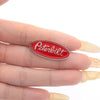 A red oval enamel lapel pin featuring the Peterbilt logo on a human finger.
