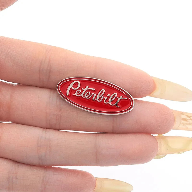 A red oval enamel lapel pin featuring the Peterbilt logo on a human finger.