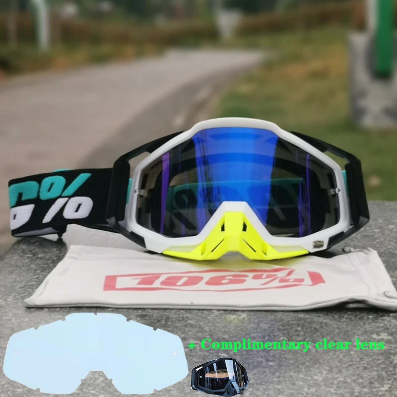 A pair of black and white motocross goggles resting on a gray surface with a clear lens insert visible.