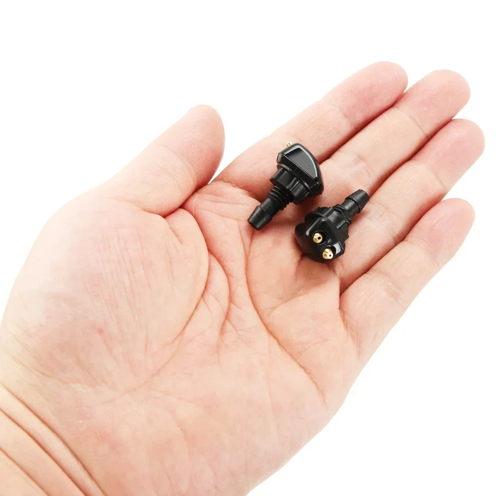 A hand holds a black universal car windshield washer nozzle with a threaded tip.