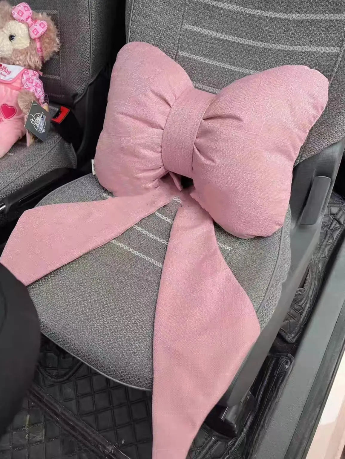 Un oreiller de cou accent rose en forme de papillon posé sur un dossier de voiture gris.