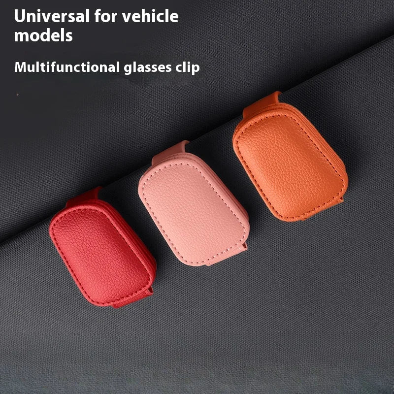 Three magnetic leather sunglasses clips in shades of orange, pink, and red resting on a dark gray fabric.