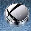 A round, silver mirror with a black 'X' design is shown resting on a wet, textured surface.