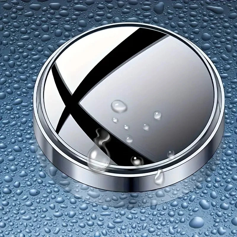 A round, silver mirror with a black 'X' design is shown resting on a wet, textured surface.