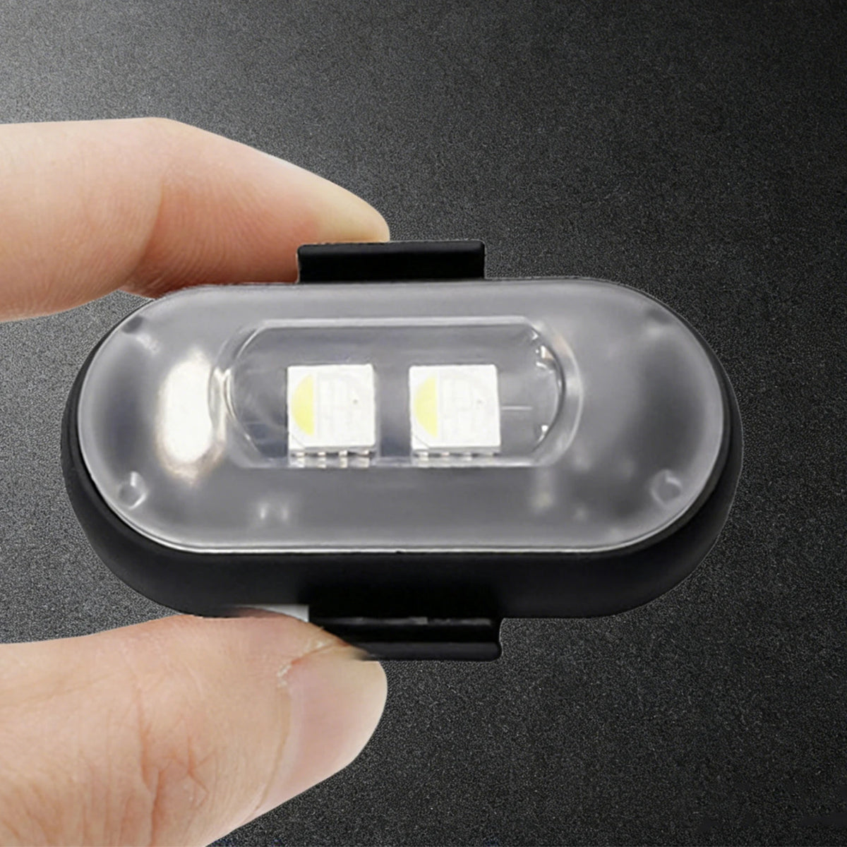Eine Hand hält eine schwarze Plastik-Stroboskoplampe mit zwei LED-Streifen, vor einem dunklen Hintergrund.