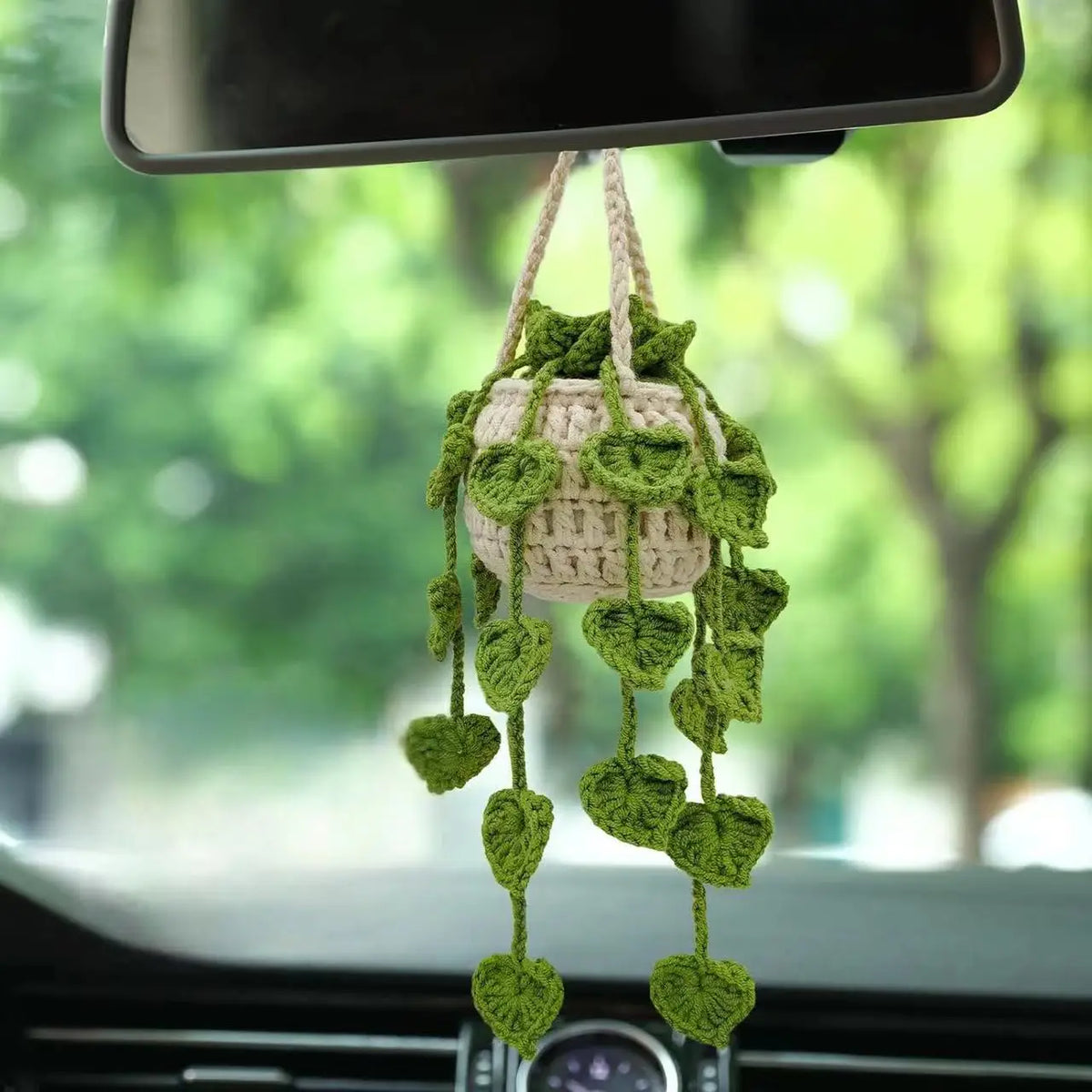 A strawberry crochet hanging decor made of light green yarn is suspended from a rearview mirror.