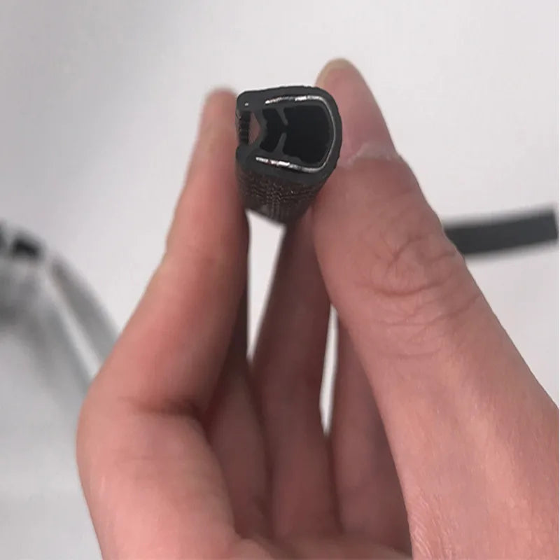 A hand holds a black rubber edge seal trim for vehicle doors and windows.