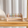 A wooden rainmaker musical toy filled with colorful glass beads, displayed on a light wooden surface.