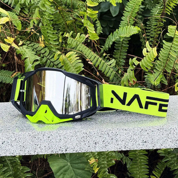 A pair of neon yellow and black NAFE motocross goggles resting on a light surface amidst green foliage.