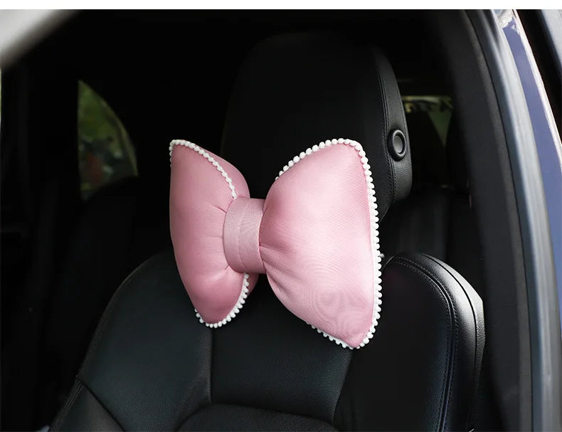 Pink satin bow design on a black car headrest pillow.