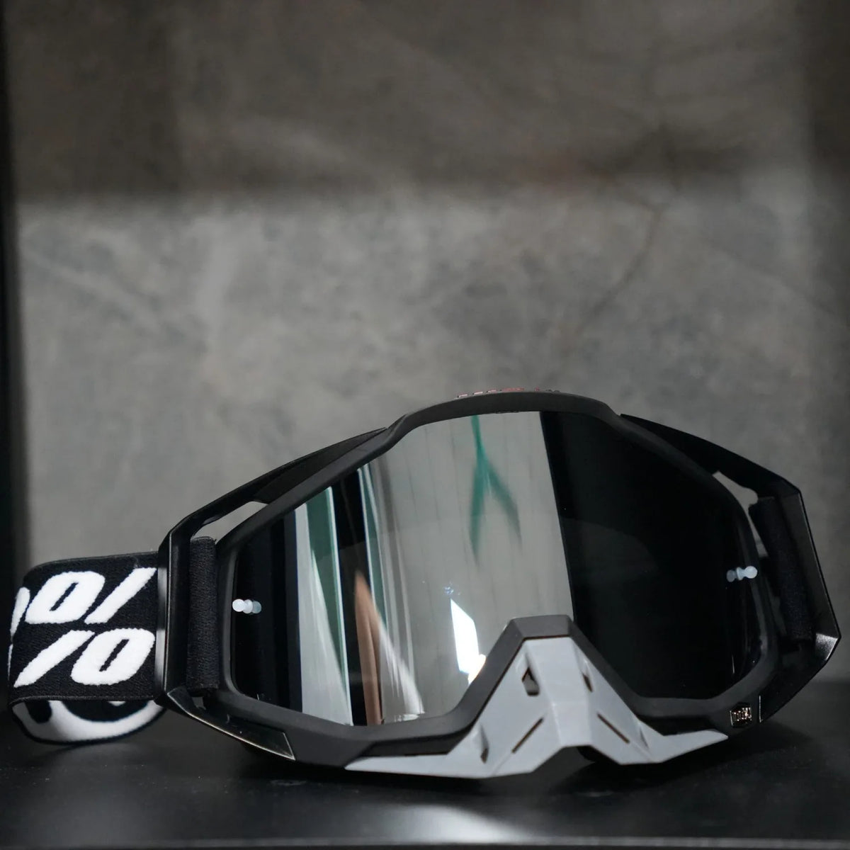 A pair of black and white high-performance motocross goggles resting on a dark surface.