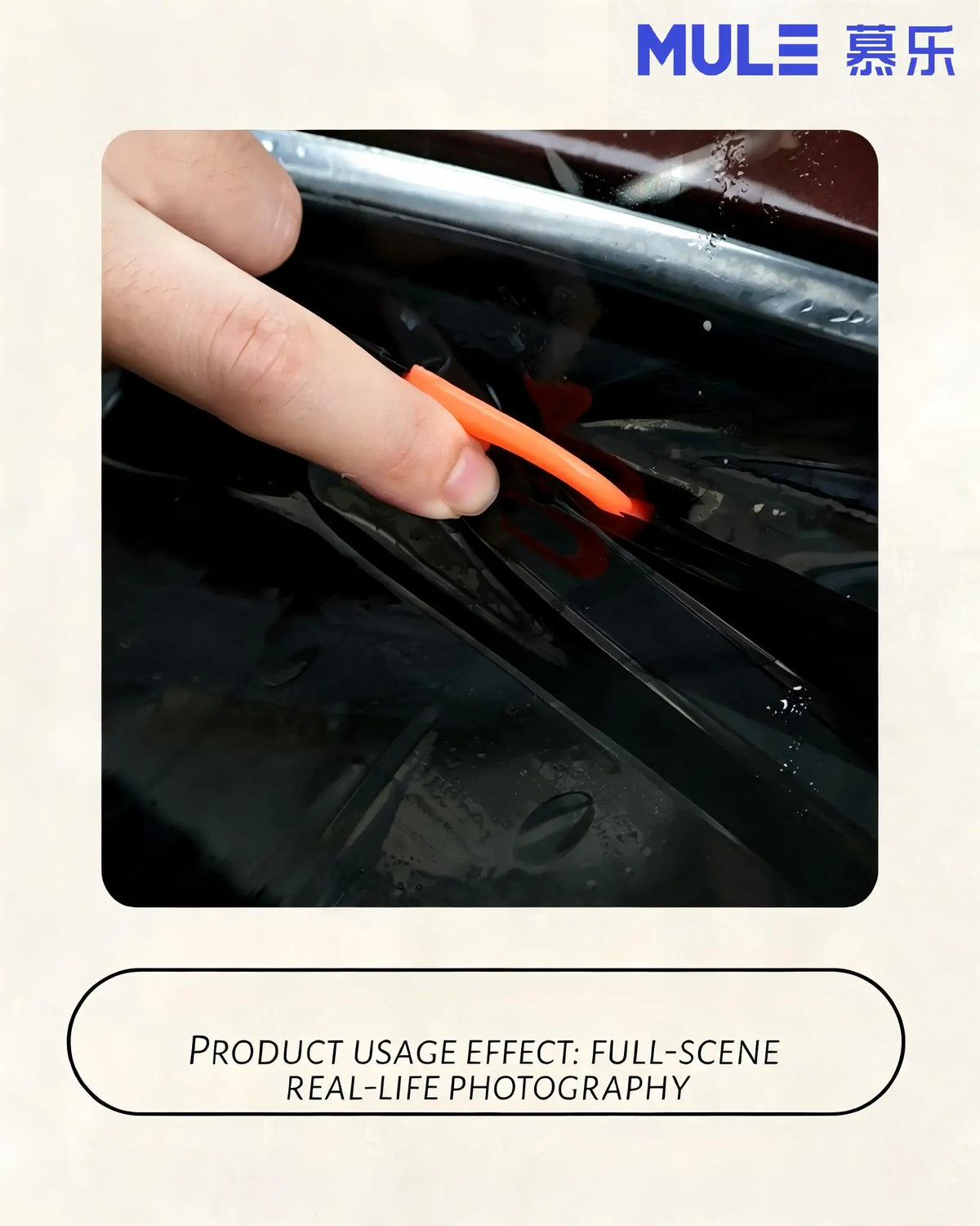 Une main utilise un cutter utilitaire orange pour couper ou appliquer du film sur une surface de voiture sombre.