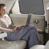 A woman sits in a car, using a laptop while a magnetic sunshade is visible on the window.