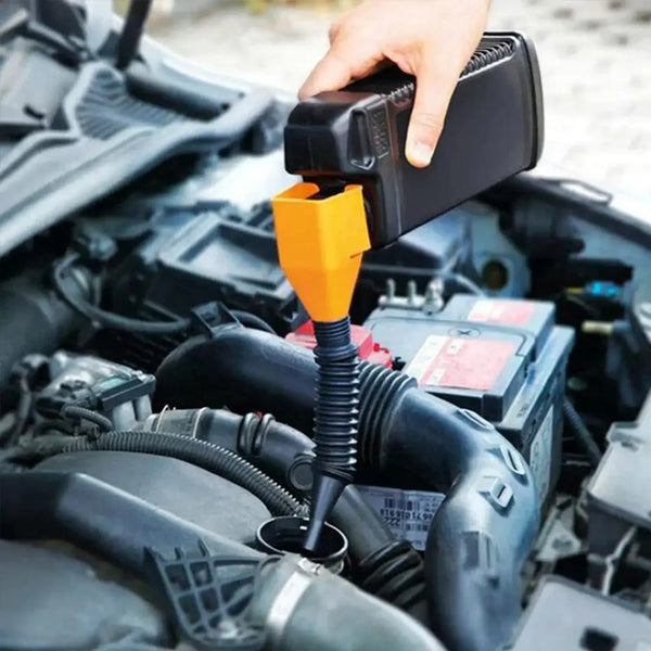 A hand is using an orange funnel to fill a fuel tank in a car engine compartment.