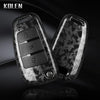 A pair of black carbon fiber car key case covers shown against a dark background.